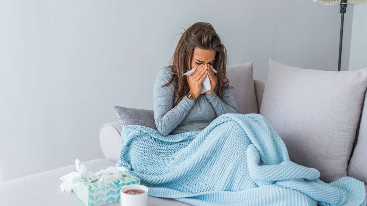 ayurvedic remedies for cold and flu season, woman with cold under a blanket on couch