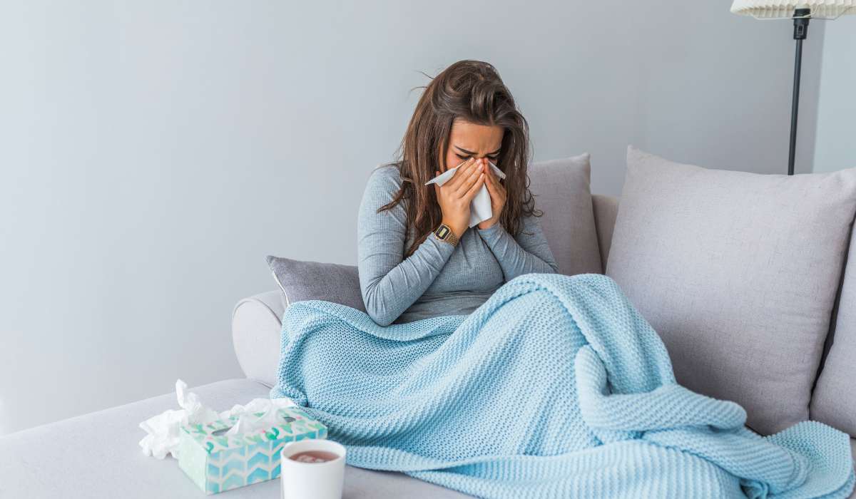 ayurvedic remedies for cold and flu season, woman with cold under a blanket on couch